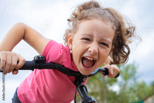 closeup portrait cheerful girl riding bicycle. mixed dentition, white teeth, smile. happy child doing sports.