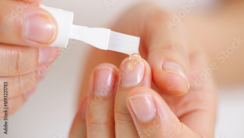 Close-up of human hands with natural nails applying clear cuticle oil with a brush for nail care