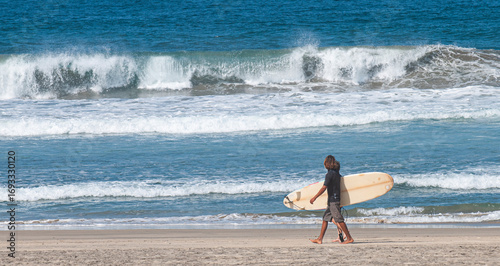 Young people with surfboards walking along the seashore at Los Cerritos beach in La Paz, Todos Santos, Baja California Sur, Mexico, on summer vacation. panoramic seascape sports