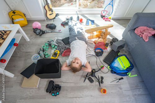 Child tidying scattered toys on the floor. Kid cleaning messy children room at home. Teen helping with household chores. Kid organizing toys in untidy playroom. Children cleaning up messy interior.