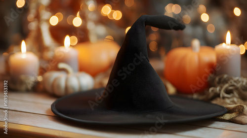 A black witch hat with candles and pumpkins blurred in the background