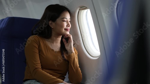 Young woman looking out airplane window during flight. Pensive passenger sitting near airplane window, gazing at expansive sky while contemplating upcoming journey.