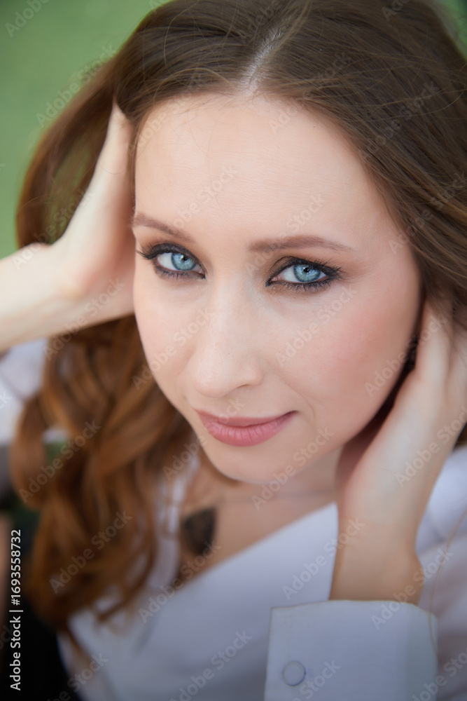 Naklejka premium Portrait of a woman with striking blue eyes and long brown hair in a relaxed pose outdoors