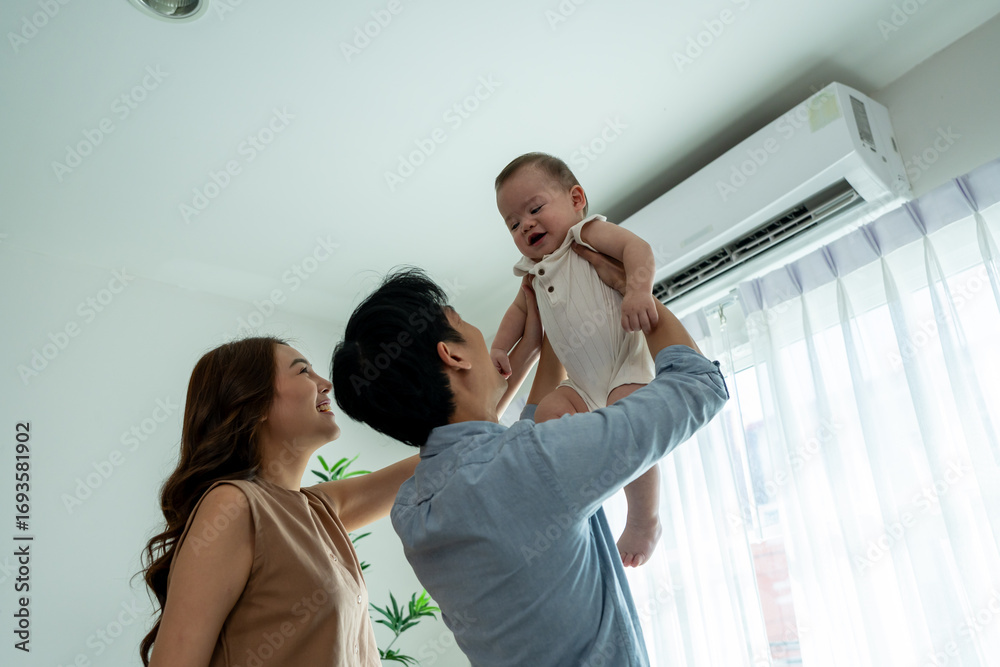 Naklejka premium Asian attractive parents gently holding their cheerful baby boy in house.