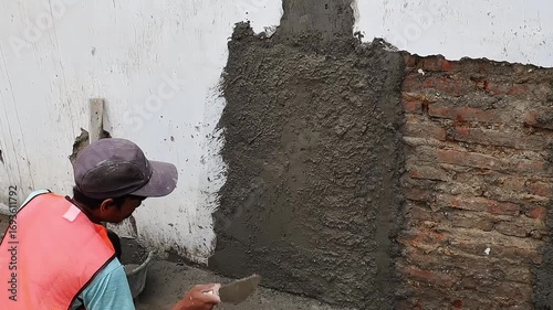 Construction worker applying wet cement plaster on wall surface during building repair and renovation