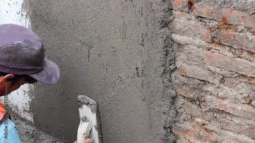 Construction worker applying wet cement plaster on wall surface during building repair and renovation