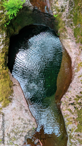 Top down view of ripples in a narrow deep pool of water in a crevice in a stone boulder. 
