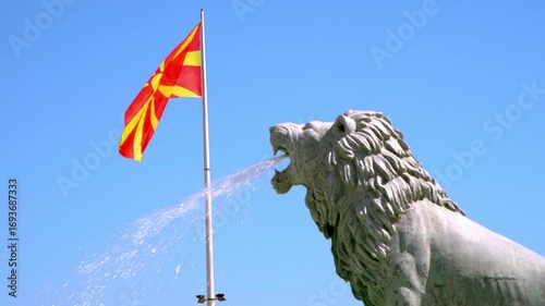 Lion statue with the colorful flag of North Macedonia in the background; fountain is located in Macedonia Square in downtown Skopje