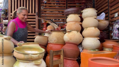 Mature Ecuadorian artisan arranging terracotta pots at a market in Cuenca, Azuay, Ecuador.
Mature afro backpacker female tourist shopping terracota pots souvenirs in a traditional street market.
