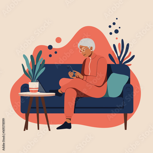A modern senior woman relaxes at home, comfortably using her smartphone on a couch next to a laptop. Represents digital literacy and leisure.