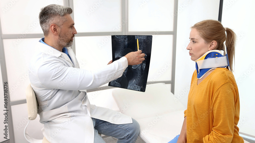 Obraz premium Adult woman with neck injury in a cervical brace during consultation with manual therapist who is looking at MRI of patient's neck