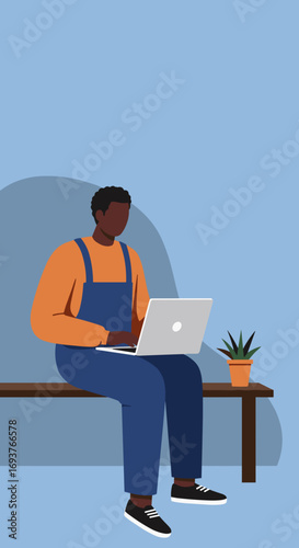 Black man in casual overalls works on a laptop, symbolizing remote work, online learning, and modern digital lifestyle in a relaxed setting.