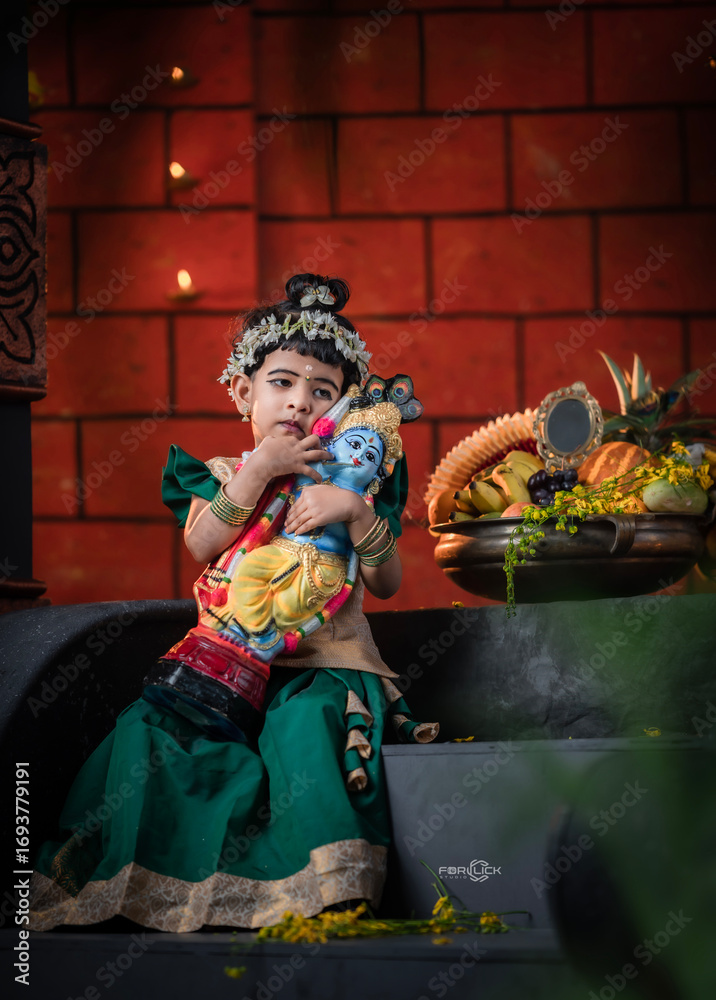 Fototapeta premium Cute Indian child dressed in traditional attire hugging Lord Krishna idol during festive celebration, Janmashtami celebration background image 2025.