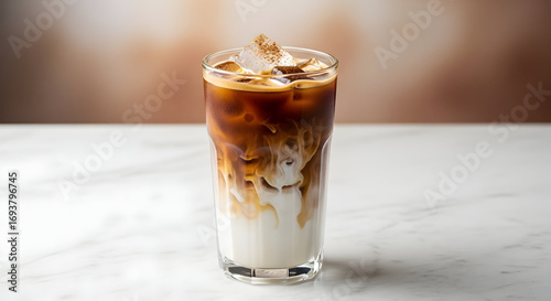 Refreshing layered iced coffee with milk and ice cubes in a tall glass, elegantly placed on a white marble surface.