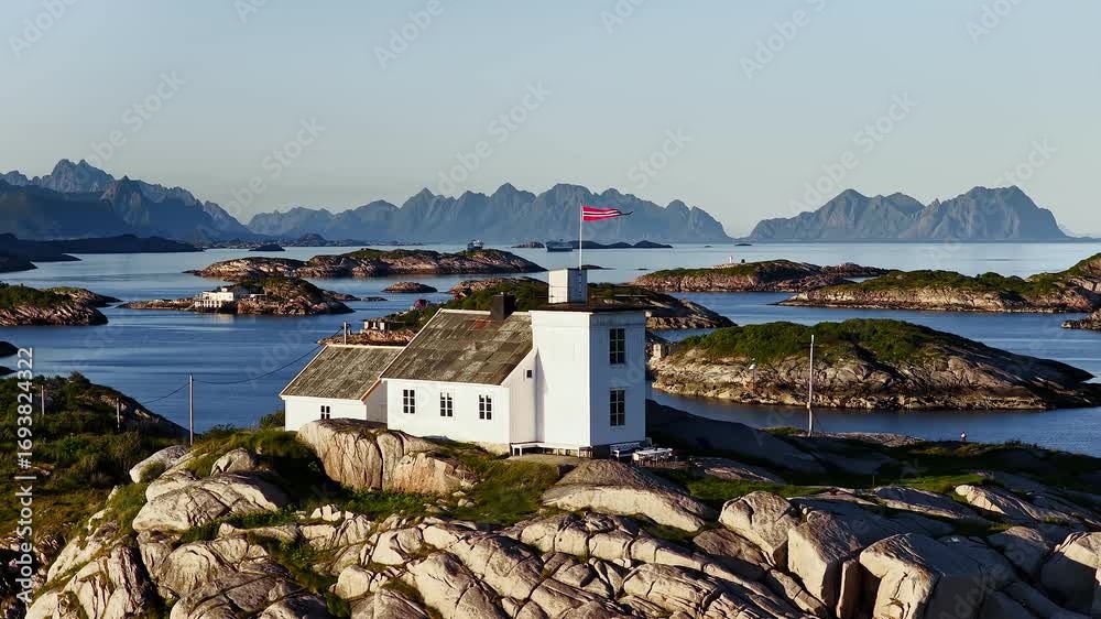 Norwegian flag waving over a white lighthouse on a rocky island in lofoten, norway