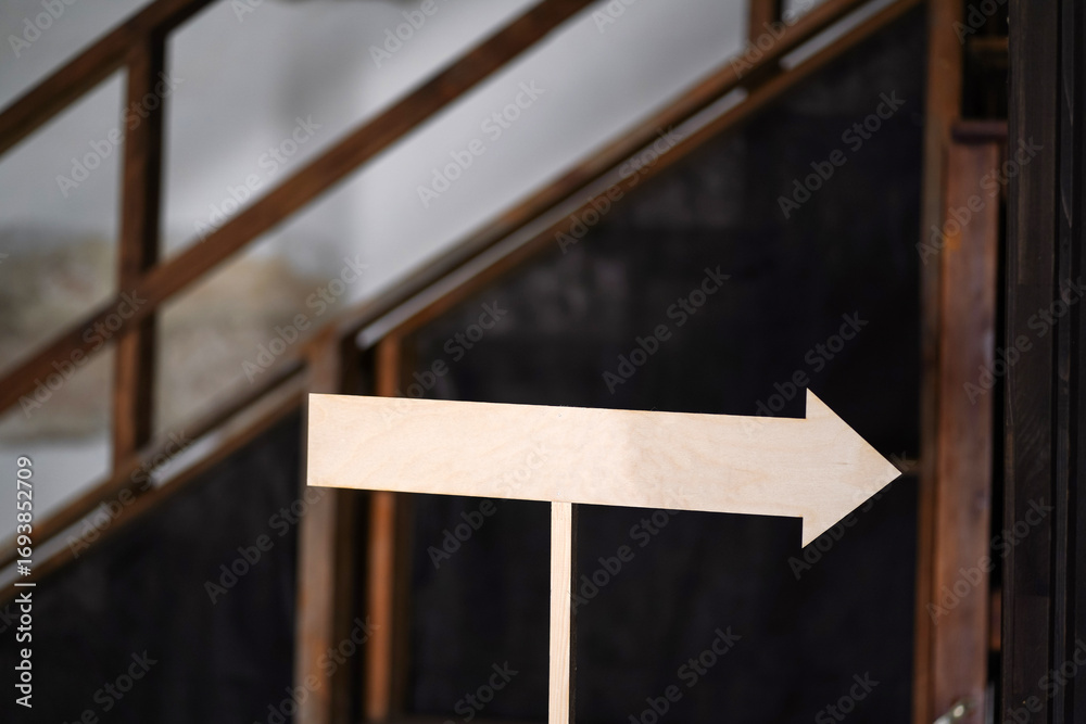 Fototapeta premium Wooden directional arrow sign indoors on blurred rustic background with stairs