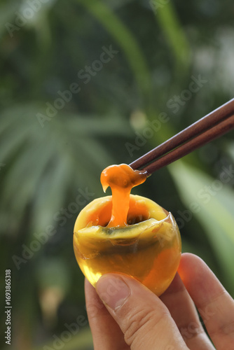 Tableau sur toile Soft-boiled egg with golden runny yolk lifted by chopsticks in hand against gree