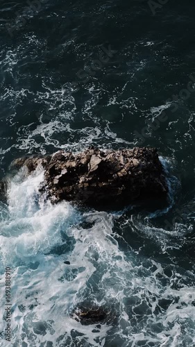 Powerful waves crash around a lone rock in the Adriatic Sea near Budva, Montenegro, at sunrise. Vertical top view 4k footage