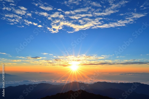 Bright sunrise over mountain range under clear blue sky with soft clouds in the morning