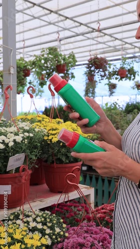 Woman choosing plant care products in flower shop greenhouse with colorful flowers