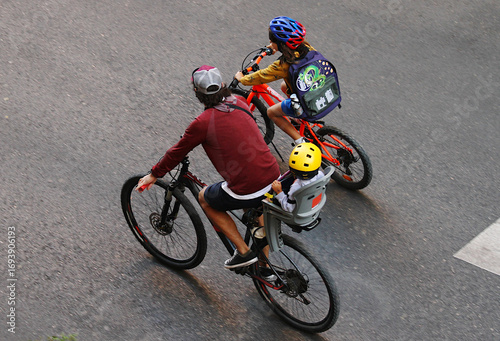 Bild auf Leinwand Vuelta al cole en bicicleta de niños y padre con casco y mochila por la carreter