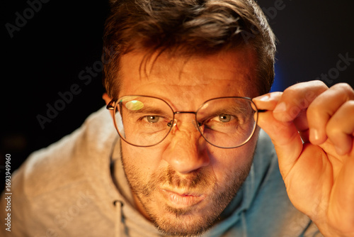Papier peint Man wearing glasses squinting and and adjusting frames, looking with interest at