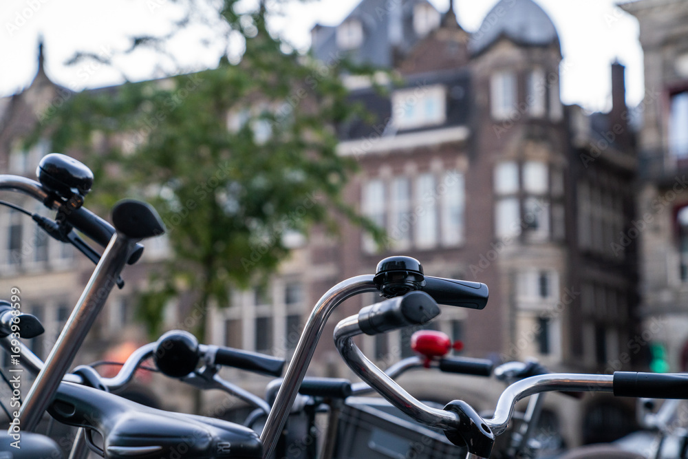 Obraz premium Close-up of bicycle handlebars and bells in a European city setting, with blurred historic architecture in the background, capturing the urban cycling culture and charm of European streets.