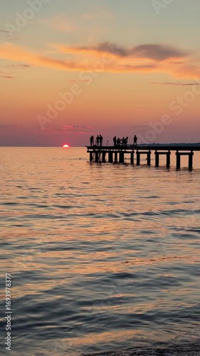 Sunset seascape with dramatic clouds, ocean waves, and a wooden pier. Warm reflections on the beach create a peaceful and atmospheric mood