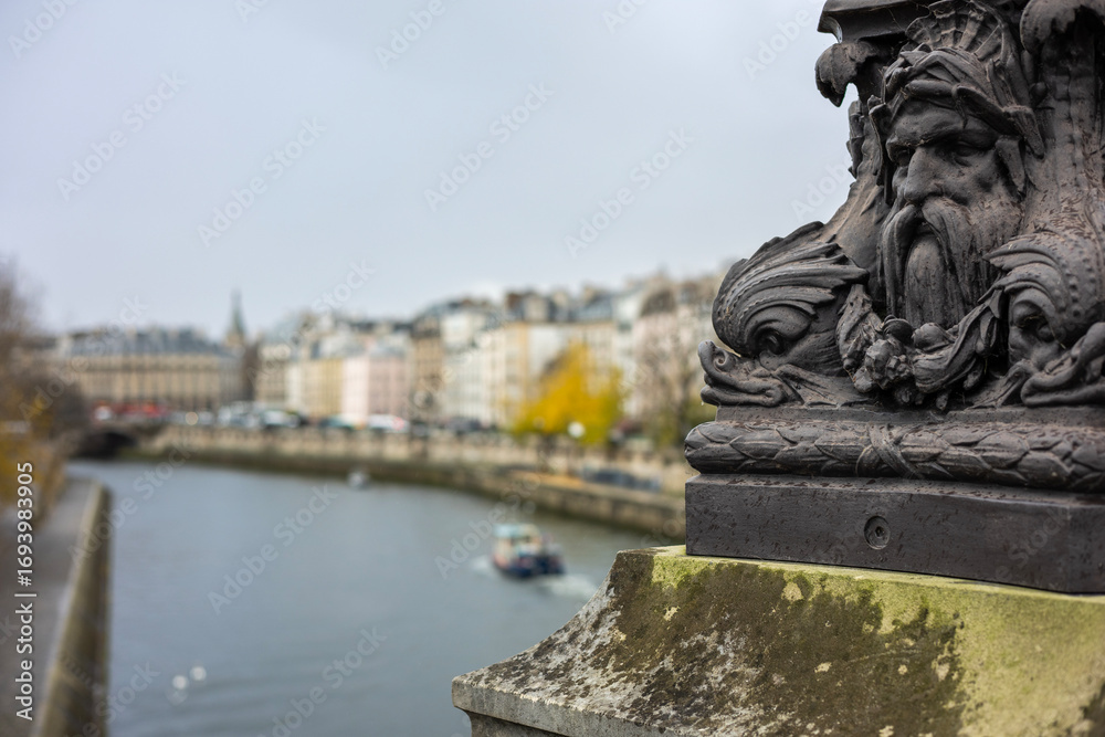 Fototapeta premium Close-up of an ornate, historic lamppost on the Pont Neuf bridge in Paris, France. The cast iron base features grotesque mascarons and sea creatures.