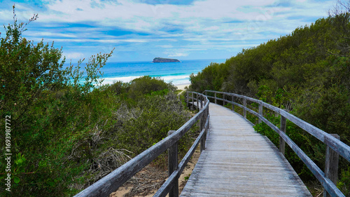 Wallpaper Mural Scenic coastal walkway leading to a serene beach with distant island view under a cloudy sky.Access to the ocean Australia. Torontodigital.ca