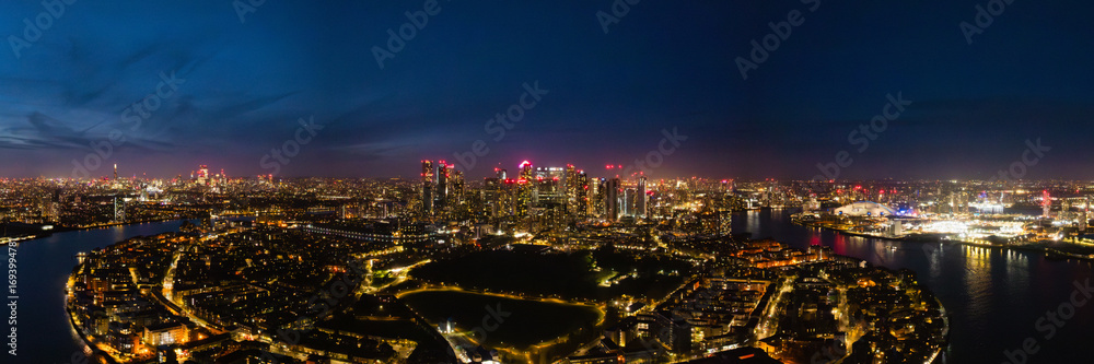 Fototapeta premium Bright city lights illuminate London's skyline at night, showcasing iconic buildings and the River Thames winding through the city.