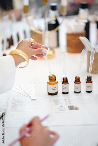 Hand using pipette with essential oil bottles on table during fragrance workshop.