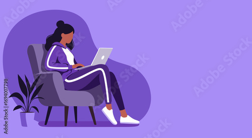 Young woman in a tracksuit comfortably working on her laptop from an armchair. Ideal for concepts of remote work, home office, and freelance lifestyle.