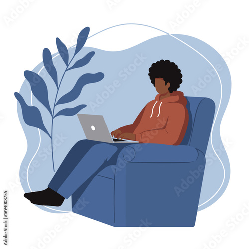 Young man comfortably working remotely on a laptop in an armchair, depicting home office, online study, or digital lifestyle.