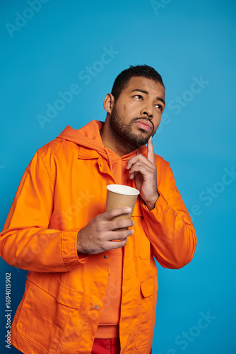 Konstfotografi Young man in vibrant orange attire reflects thoughtfully in a studio setting