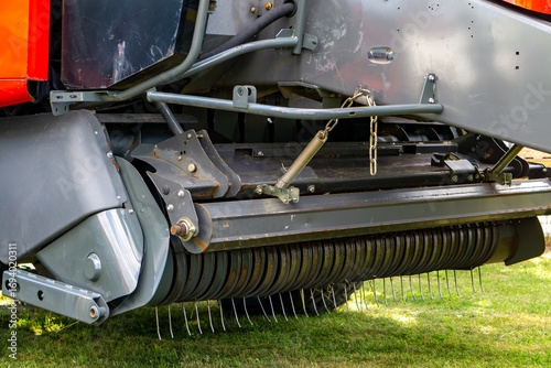 Photos Close-up of round baler with pickup and metal tines for hay collection, technical detail of modern agricultural machine used during harvest