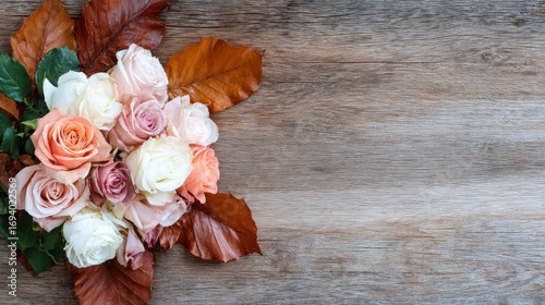 A floral bouquet of pastel roses and autumn leaves sits on a weathered wooden surface