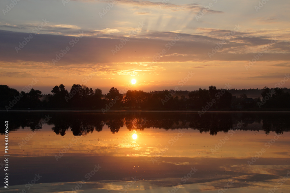 Naklejka premium Beautiful moments of sunrise. Shot from the surface of the lake, the shore and trees against the beautiful sky. Morning fog. Reflection on the surface of the water.