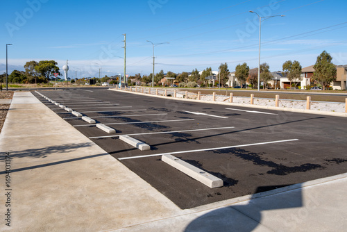 Empty asphalt parking lot in a suburban neighborhood of Australia, with marked bays, concrete wheel stops, and surrounding residential houses. Urban planning, public infrastructure, and transportation