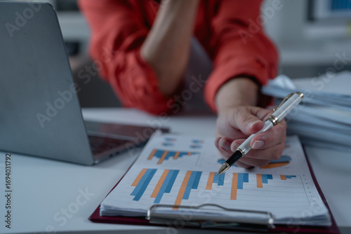 Tableau sur toile Businesswoman analyzing financial charts and graphs while using a laptop and pen