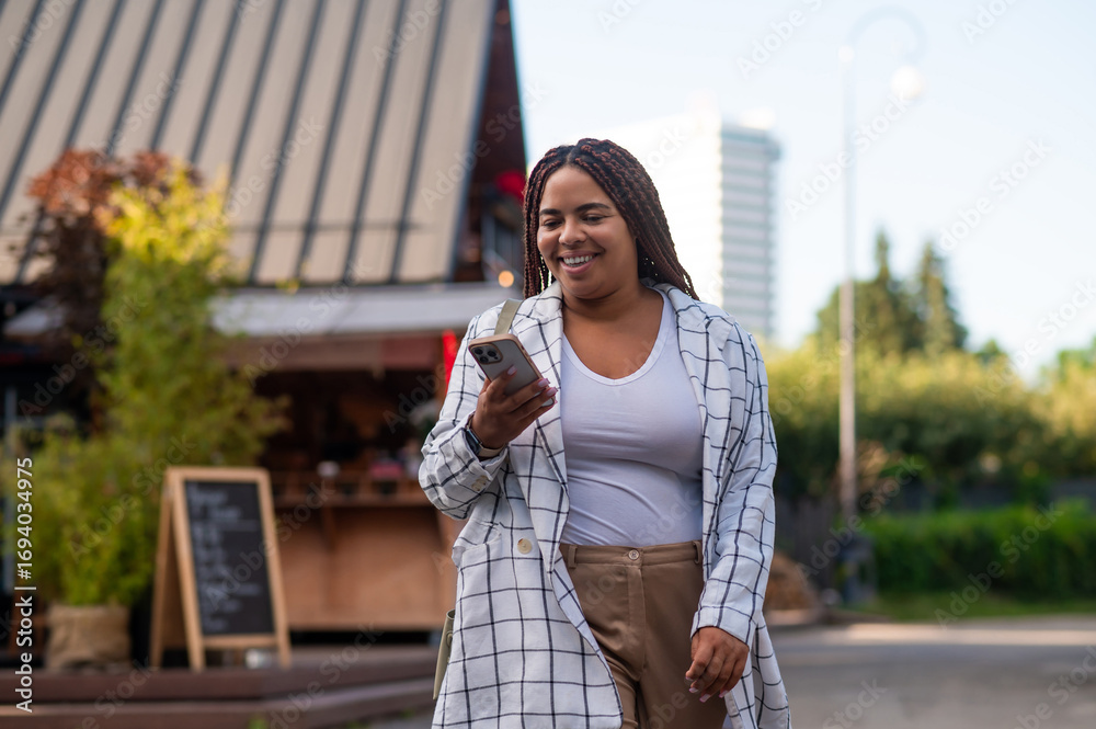Fototapeta premium Curvy woman checking smartphone while walking outdoors