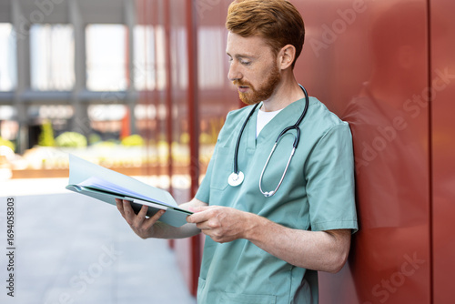 Man in green uniform leaning on wall with open patient records
