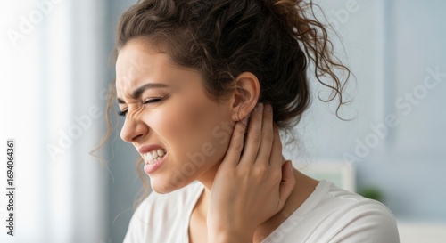 A woman winces in pain her hand gripping her neck Her teeth are clenched eyes shut and hair is piled on top of her head