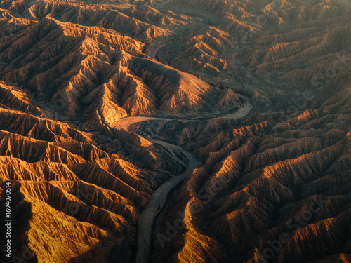 Aerial view of a river snaking through rugged, sun-baked canyons, the landscape painted in hues of ochre and deep shadow, Ak Say, Issyk-Kul Region, Kyrgyzstan.