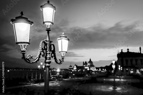 Lampione storico acceso al tramonto in Piazza San Marco a Venezia, simbolo di fascino romantico e atmosfera veneziana.
