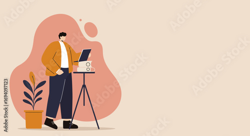 Young man working remotely on a laptop, standing by a tripod with books and coffee. Ideal for concepts of online education, digital business, and home office productivity.