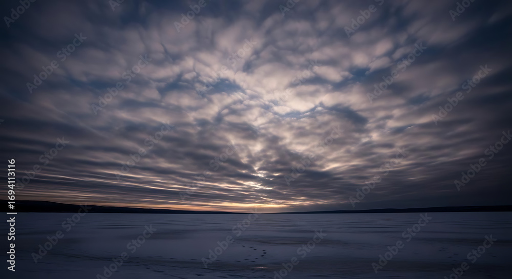 Fototapeta premium Expansive cloudy sky over a flat snowy landscape at dusk with a horizon glow and subdued colors