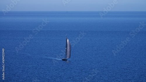 A lone sailboat navigates the expansive, tranquil waters, leaving a subtle wake behind it on a bright day