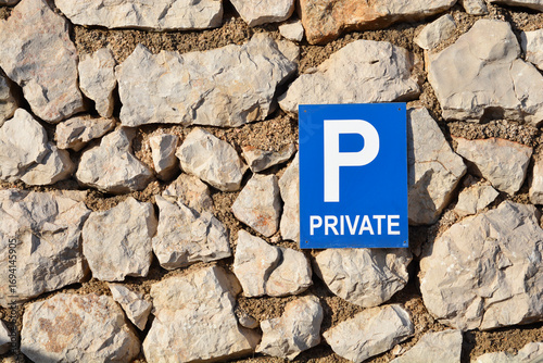 A blue and white private parking sign is mounted on a traditional stone wall, creating a contrast of man-made and natural elements