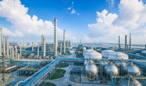 Panoramic view of oil refinery and chemical plant with complex pipelines, storage tanks and a bridge in the background.